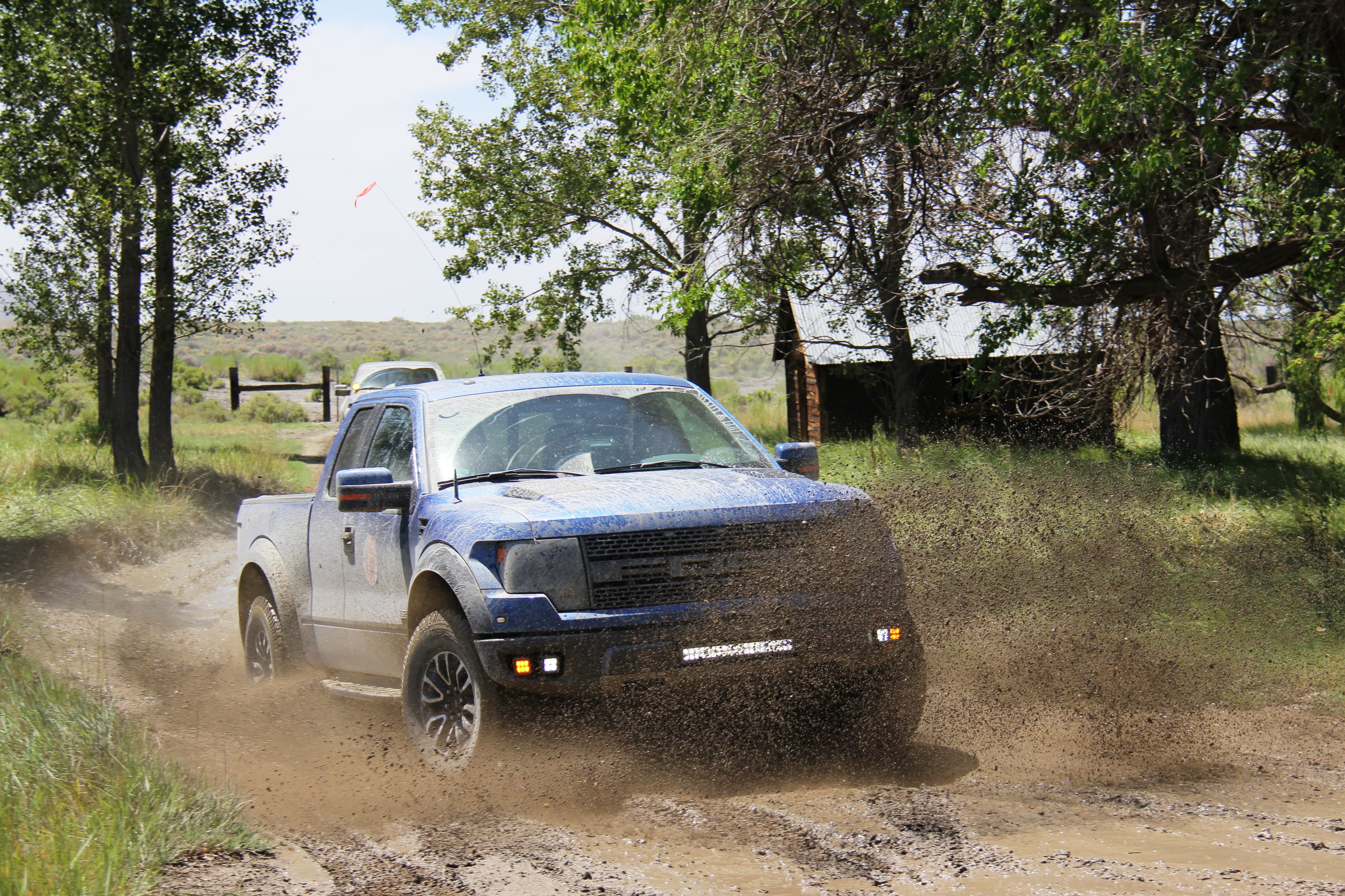 Blue first-gen SVT Raptor SuperCab throwing a rooster tail of mud down a two-track outside Fernley, Nevada