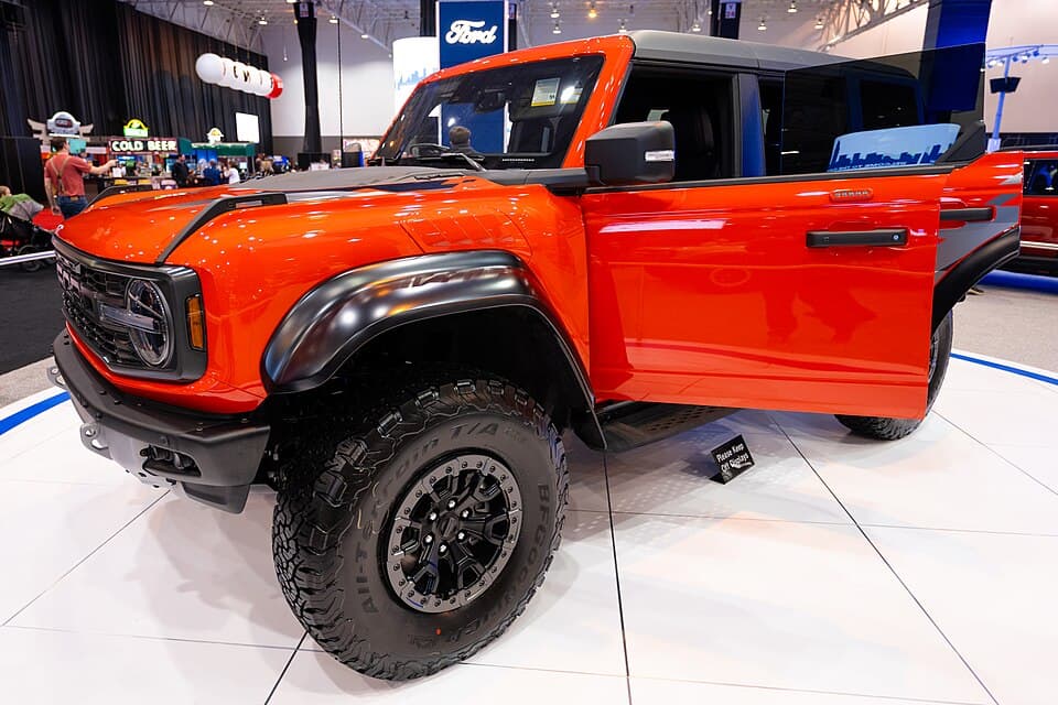 Code Orange Bronco Raptor in profile at the 2024 Cleveland Auto Show, doors and roof removed — clean look at the fender flares and rocker protection.
