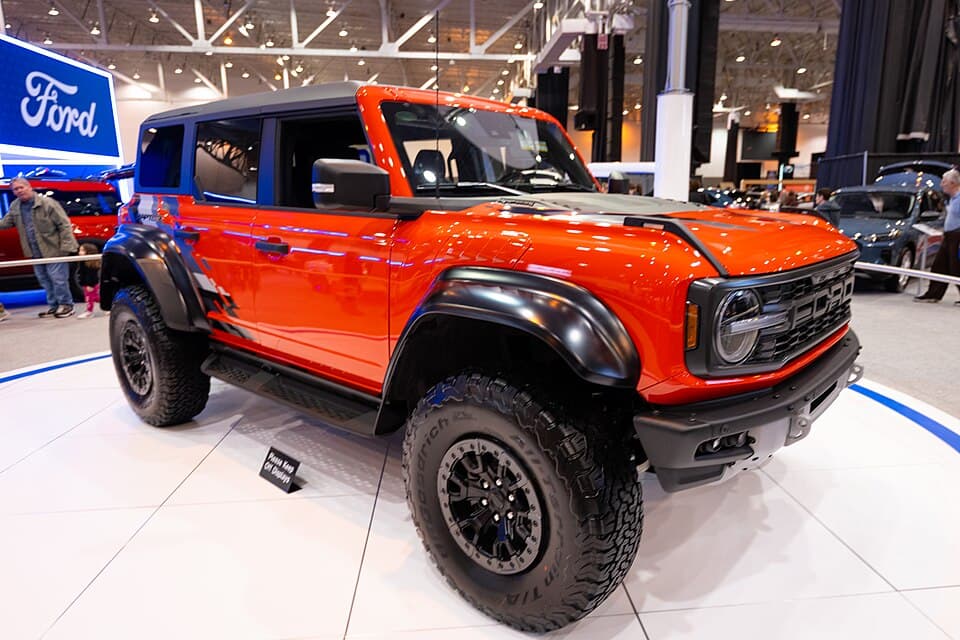 Code Orange Bronco Raptor on the Ford stand at the 2024 Cleveland Auto Show, front three-quarter with the doors removed.