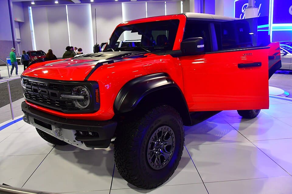 Red Bronco Raptor at the 2024 Washington Auto Show with the doors open, front three-quarter — interior and roll structure visible.