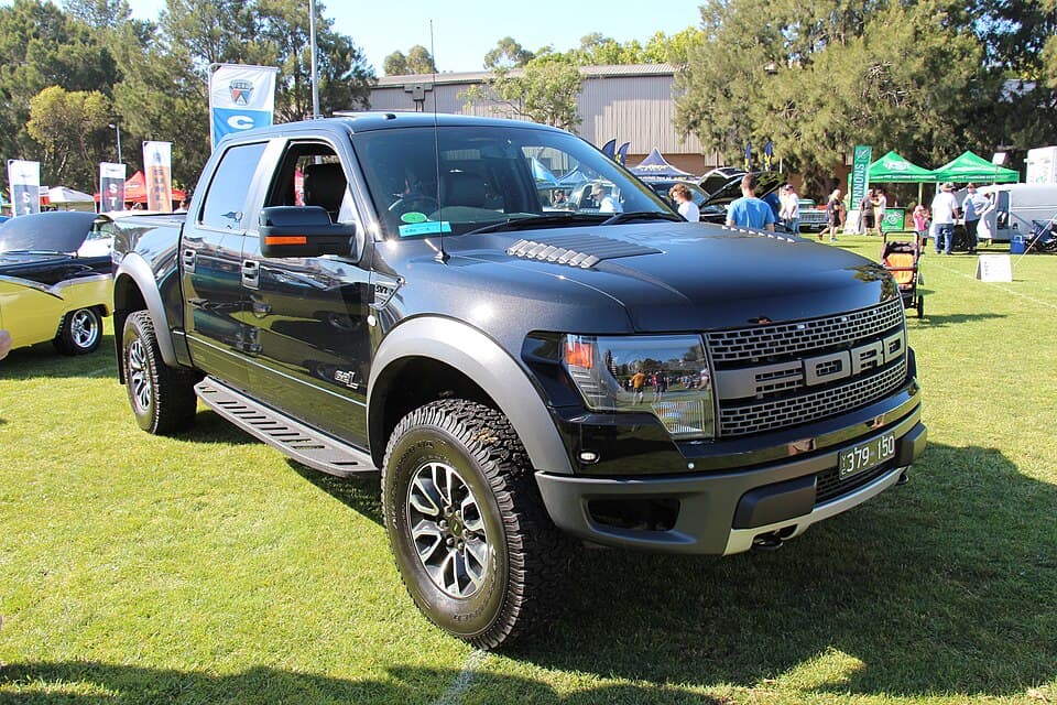 Black 2014 F-150 SVT Raptor SuperCrew on grass at an Australian show, front three-quarter, sitting on stock 35s.