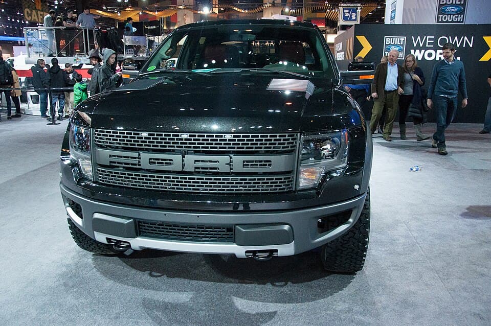 2014 SVT Raptor shot head-on under show lights, giving a clean look at the amber grille marker lights and the front skid plate.