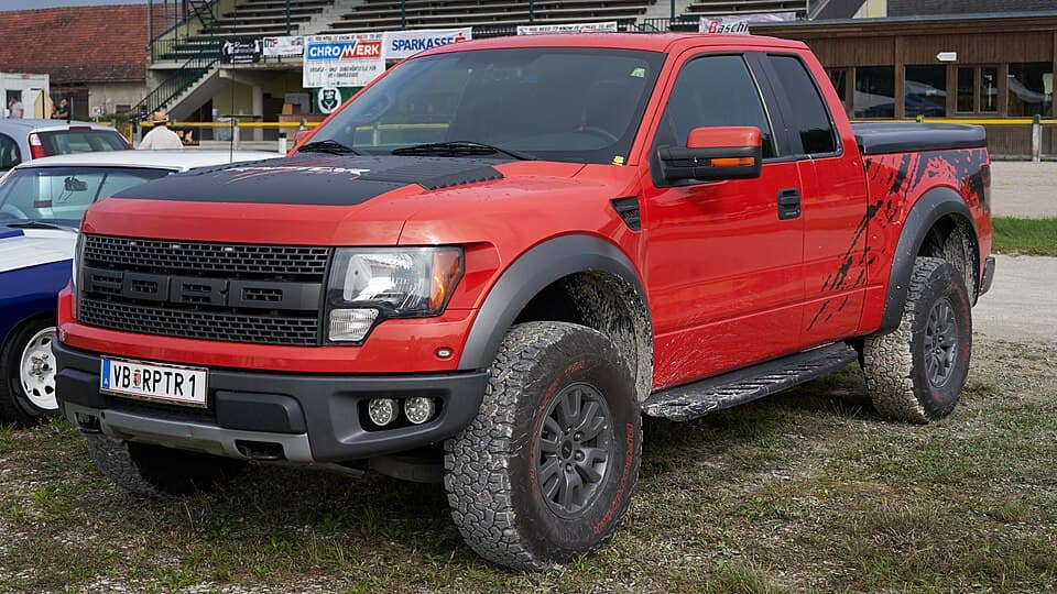 Red first-gen SVT Raptor SuperCab with black hood and bedside splatter graphics, front three-quarter on grass at the Austrian 500 US-Car Days.