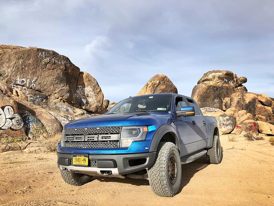 Blue first-gen Raptor SuperCrew parked among graffiti-covered boulders off Old Woman Springs Road in the California high desert.