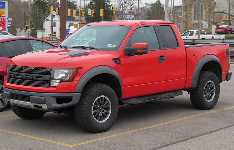 2010 SVT Raptor SuperCab in Molten Orange Metallic Tri-Coat, front three-quarter in a Pennsylvania parking lot, wearing the early smooth-surround grille.