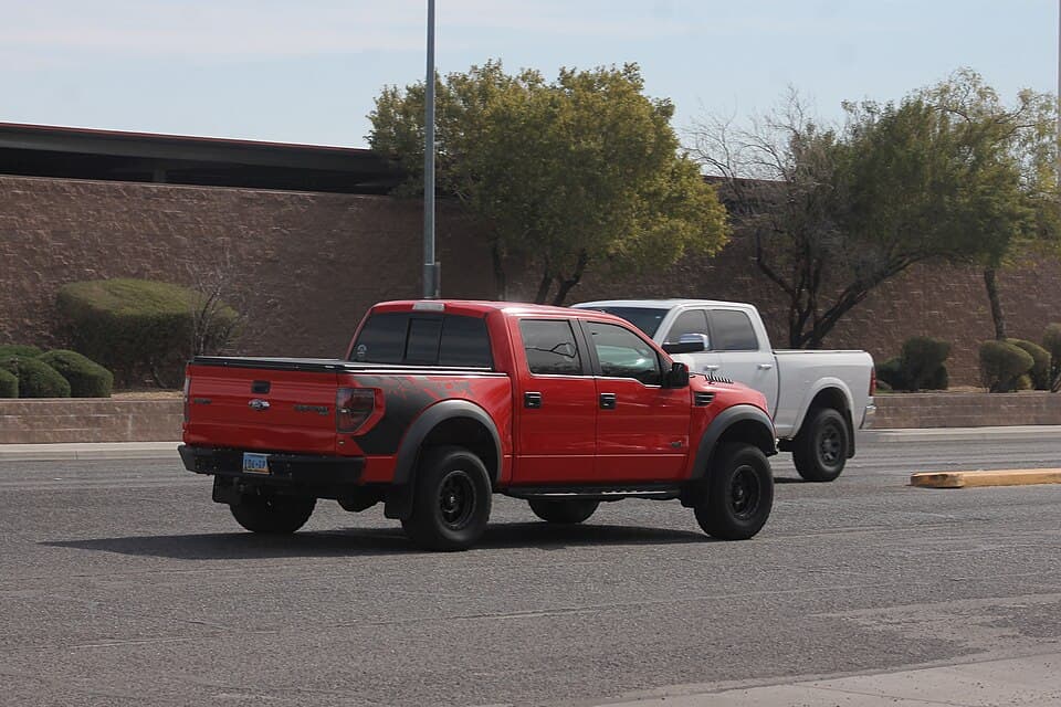 Red 2013 SVT Raptor SuperCrew moving away from the camera in Las Vegas traffic, showing the bedside RAPTOR graphic and the flared rear arches.