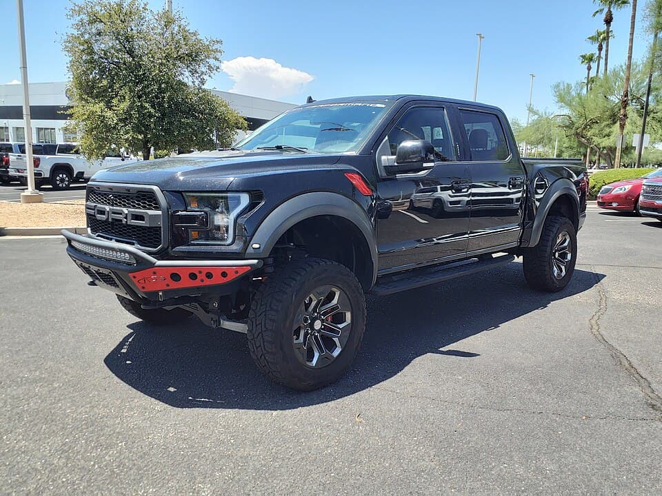 Black 2019 Raptor SuperCrew with red bumper accents and a light bar, side three-quarter on a dealer lot in Mesa, Arizona.