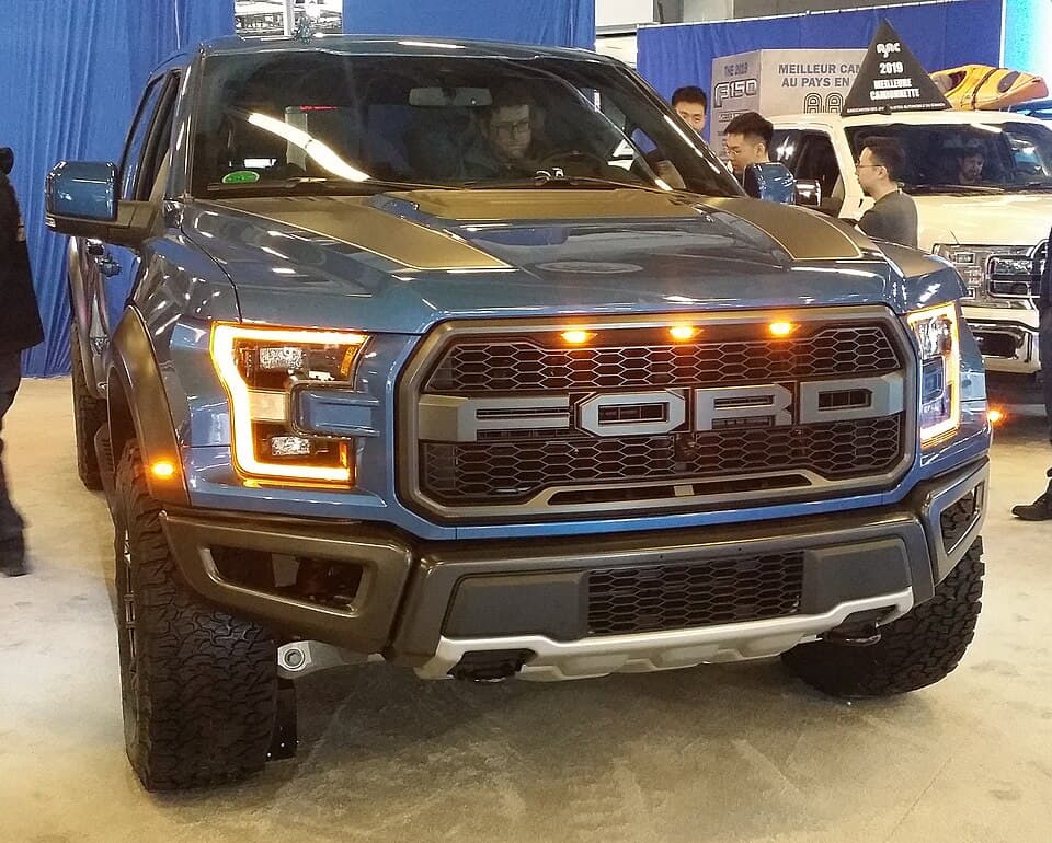 2019 Raptor on the stand at the Montréal International Auto Show, front three-quarter under show lighting with the running lights lit.