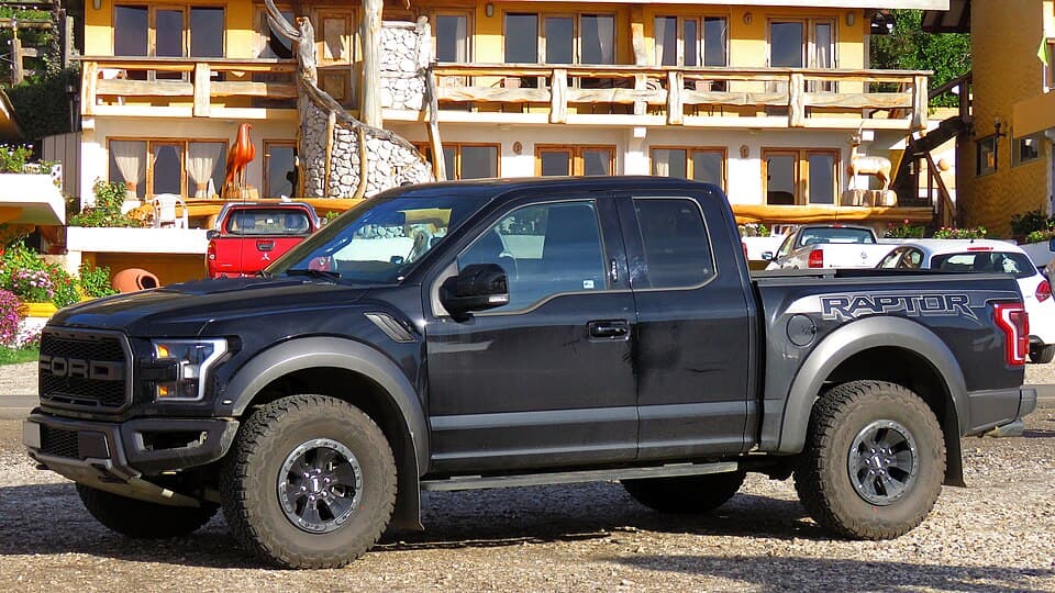 Black 2018 Raptor SuperCab with the RAPTOR bedside decal, front three-quarter parked outside a lodge.