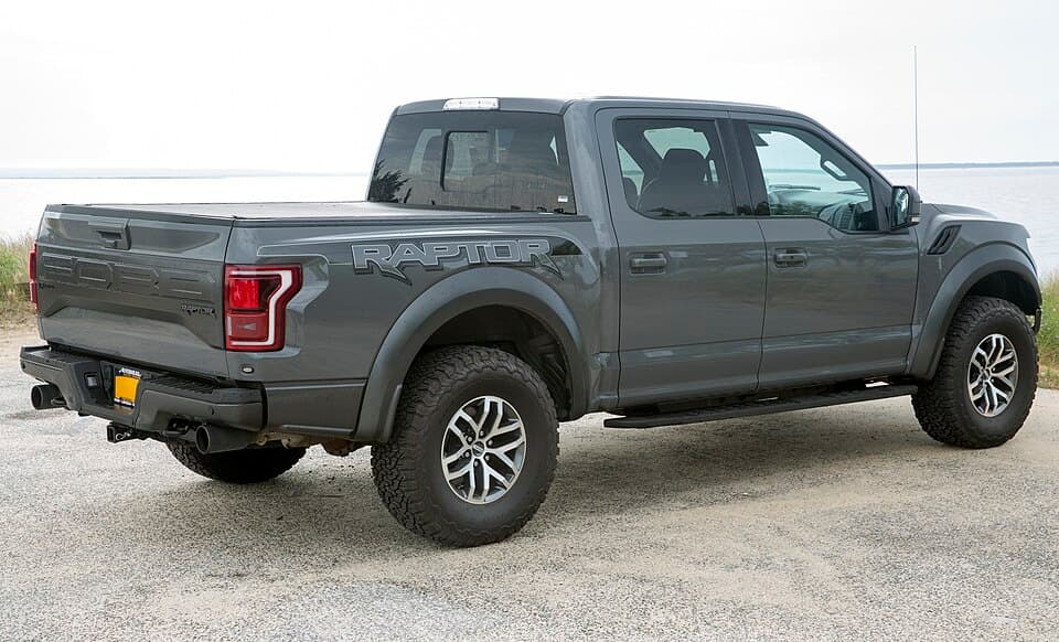 2018 Raptor SuperCrew in Lead Foot grey, rear-right three-quarter — bedside RAPTOR lettering and the rear flare over a 35-inch tyre.