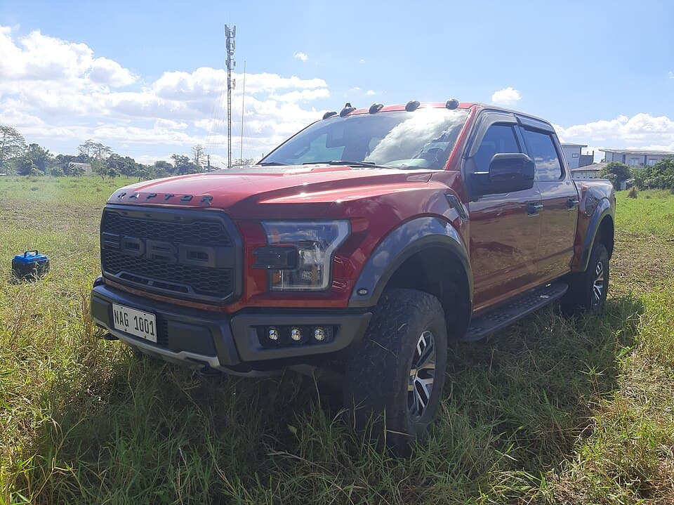 Red second-gen Raptor with roof-mounted marker lights and auxiliary bumper lights, parked in a grass field in Nueva Ecija, Philippines.