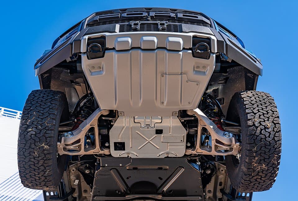 The underside of a second-gen Raptor on a display ramp: full front skid plate, independent front suspension and the exposed control arms. Rare view of what actually takes the hits.