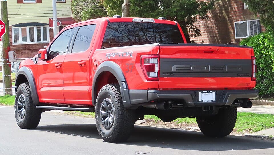 Code Orange 2021 Raptor from the rear three-quarter in Queens, showing the stamped FORD tailgate and the five-link rear end.