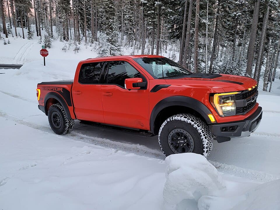 Code Orange third-gen Raptor on a snow-covered forest road, front three-quarter — a rare cold-weather shot of the P702.